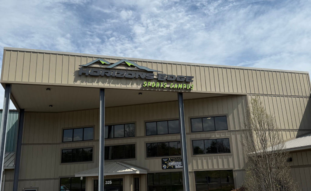 Exterior of the Horizons Edge Sports Campus facility featuring a large mounted logo with a mountain graphic above the entrance of a modern multi-story building."